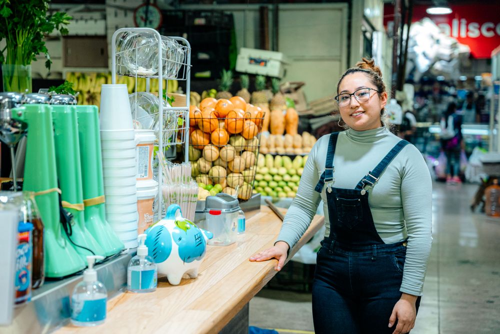 Joven sonriendo en su puesto de frutas y jugos en el mercado